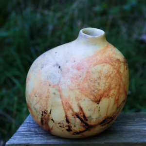 Large saggar fired ceramic vase with organic smoke patterns, displayed outdoors on wooden surface.