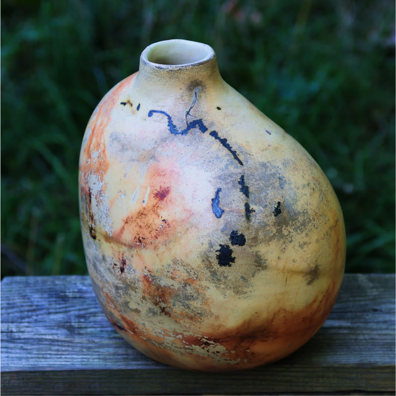 Asymmetrical saggar vase on a rustic bench, showing surface created by organic firing.