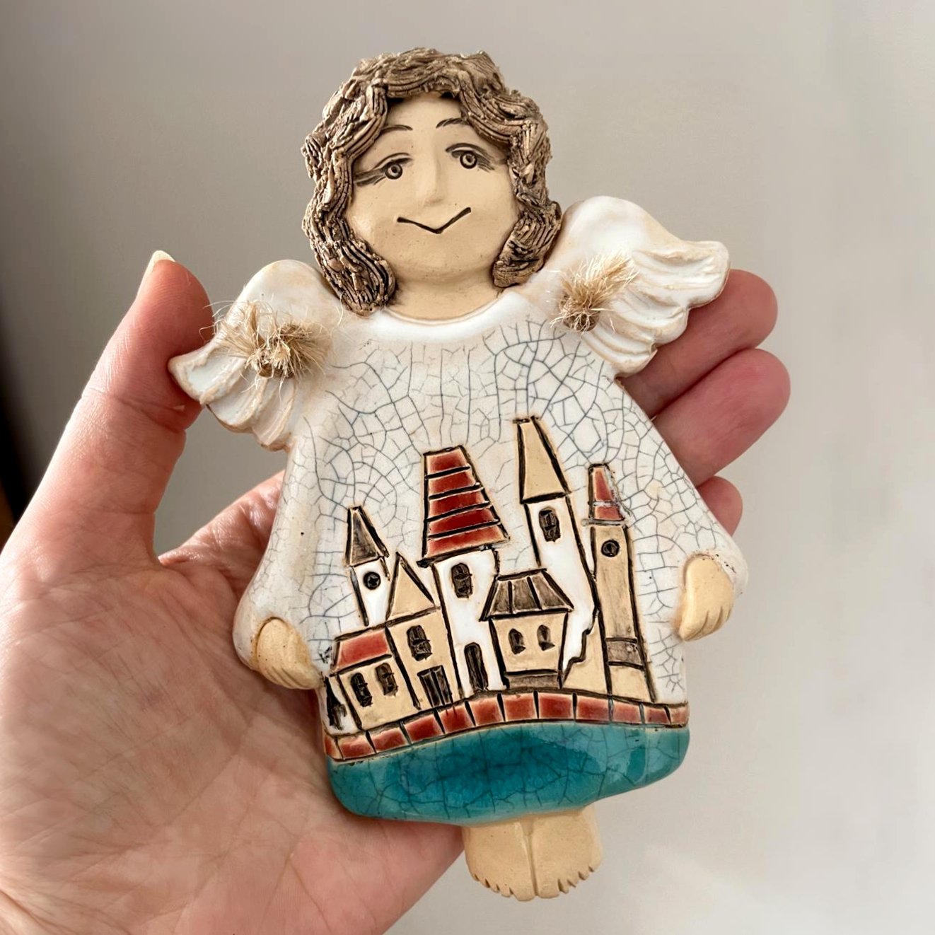 Handmade ceramic wall angel held in hand for size reference