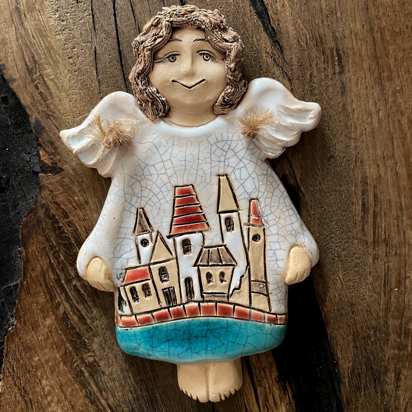Handmade ceramic wall angel with little town on wooden background