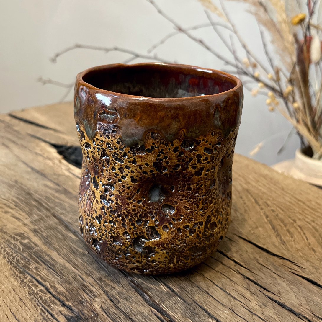 Handmade ceramic yunomi tea cup with lava texture glaze on wooden table
