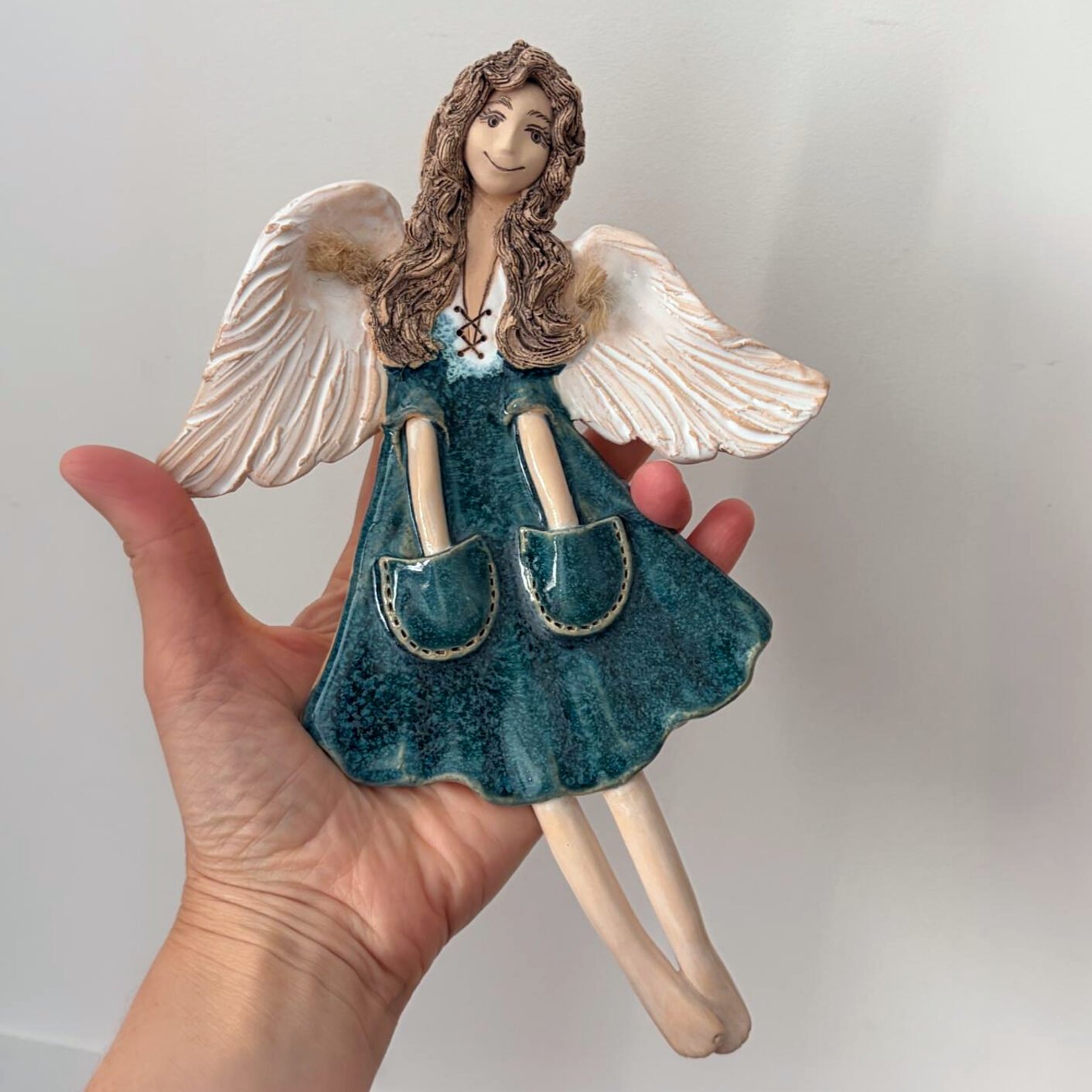 Handmade ceramic angel wall hanging shown in hand for size