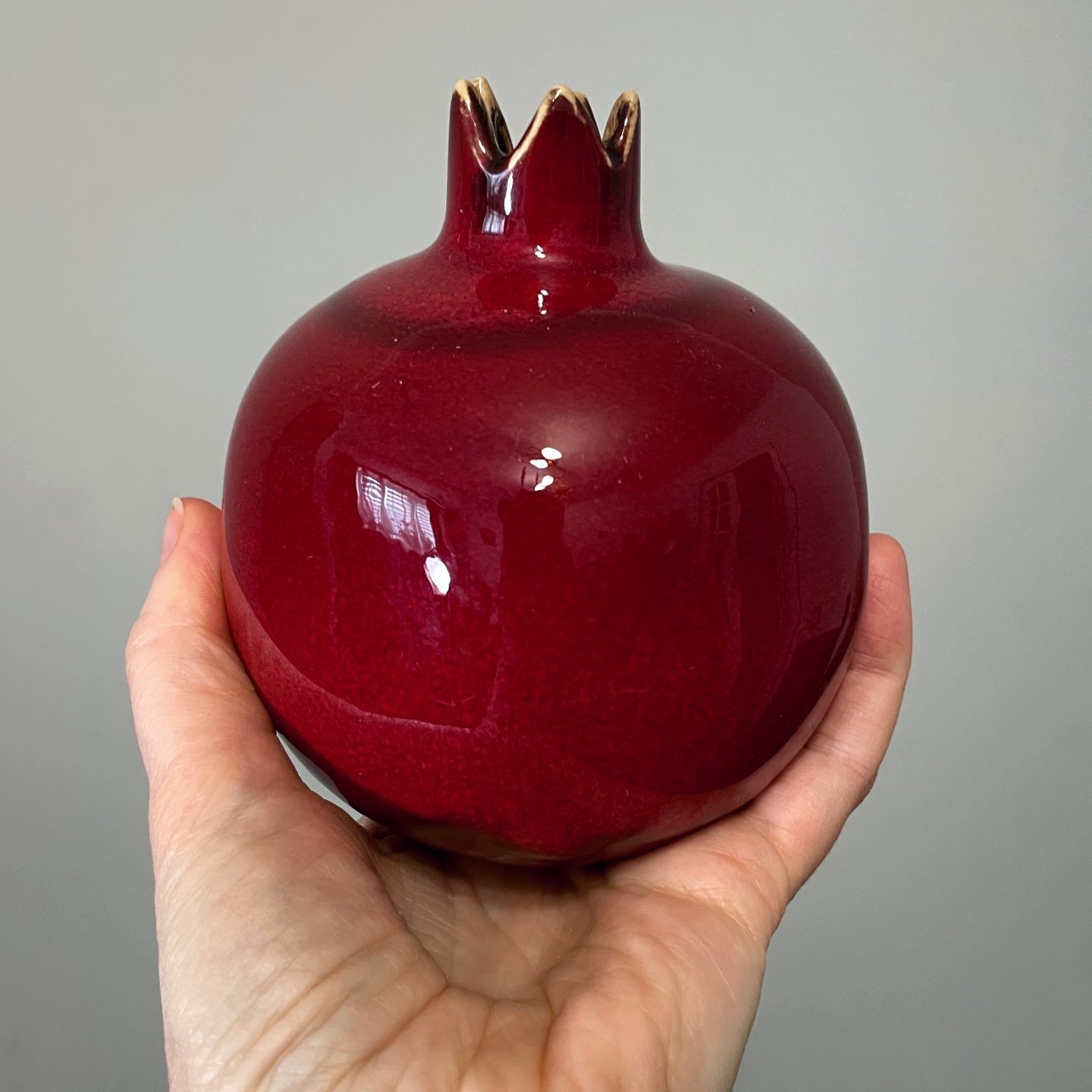 handmade red ceramic pomegranate sculpture held in hand, pottery fruit object