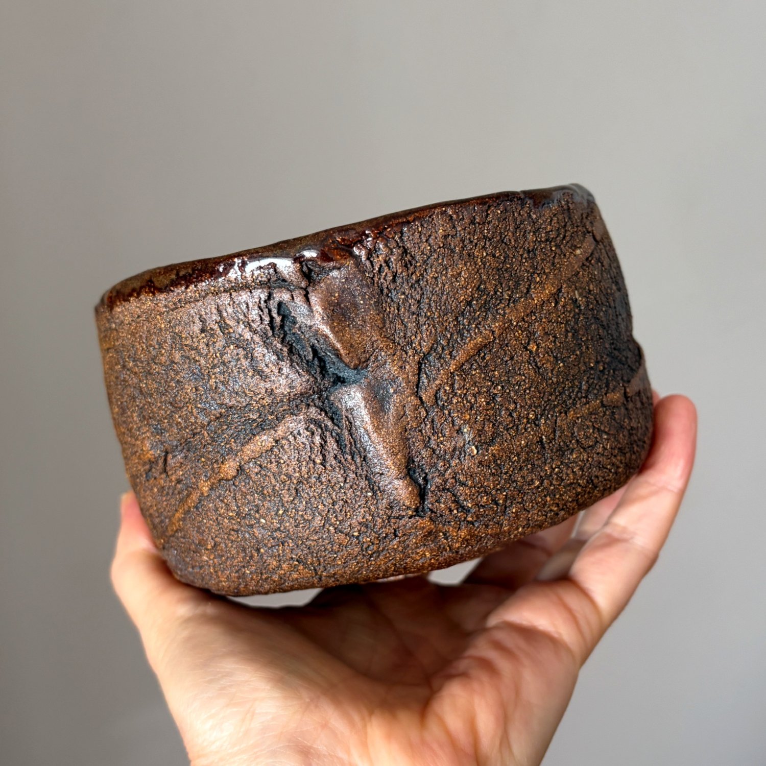 Textured stoneware tea bowl held in hand for size reference