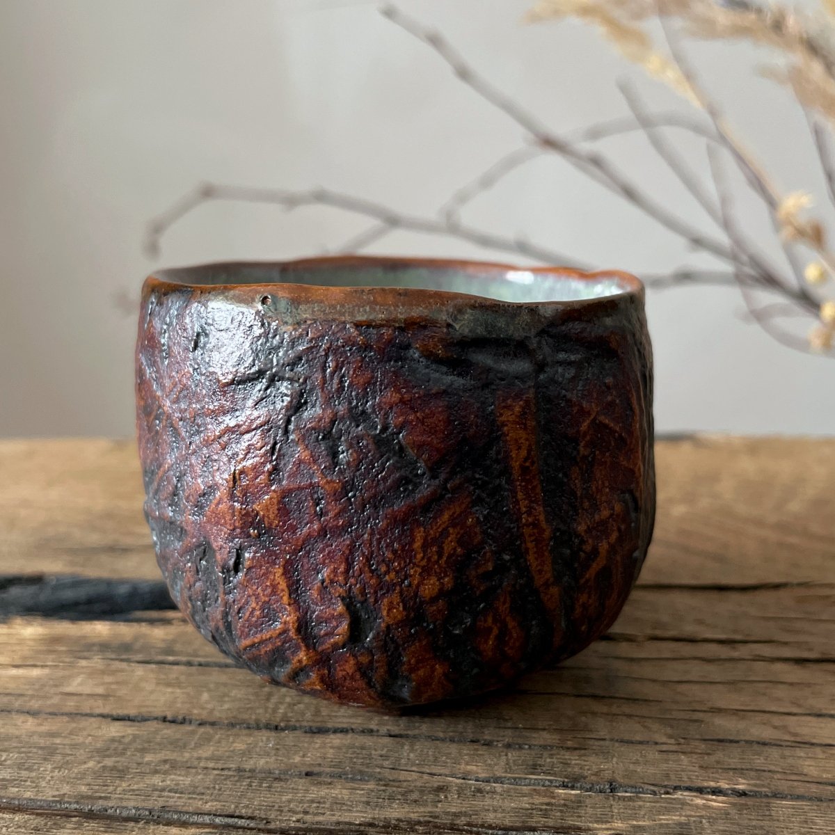 Textured ceramic yunomi cup in red and brown glaze on wooden table