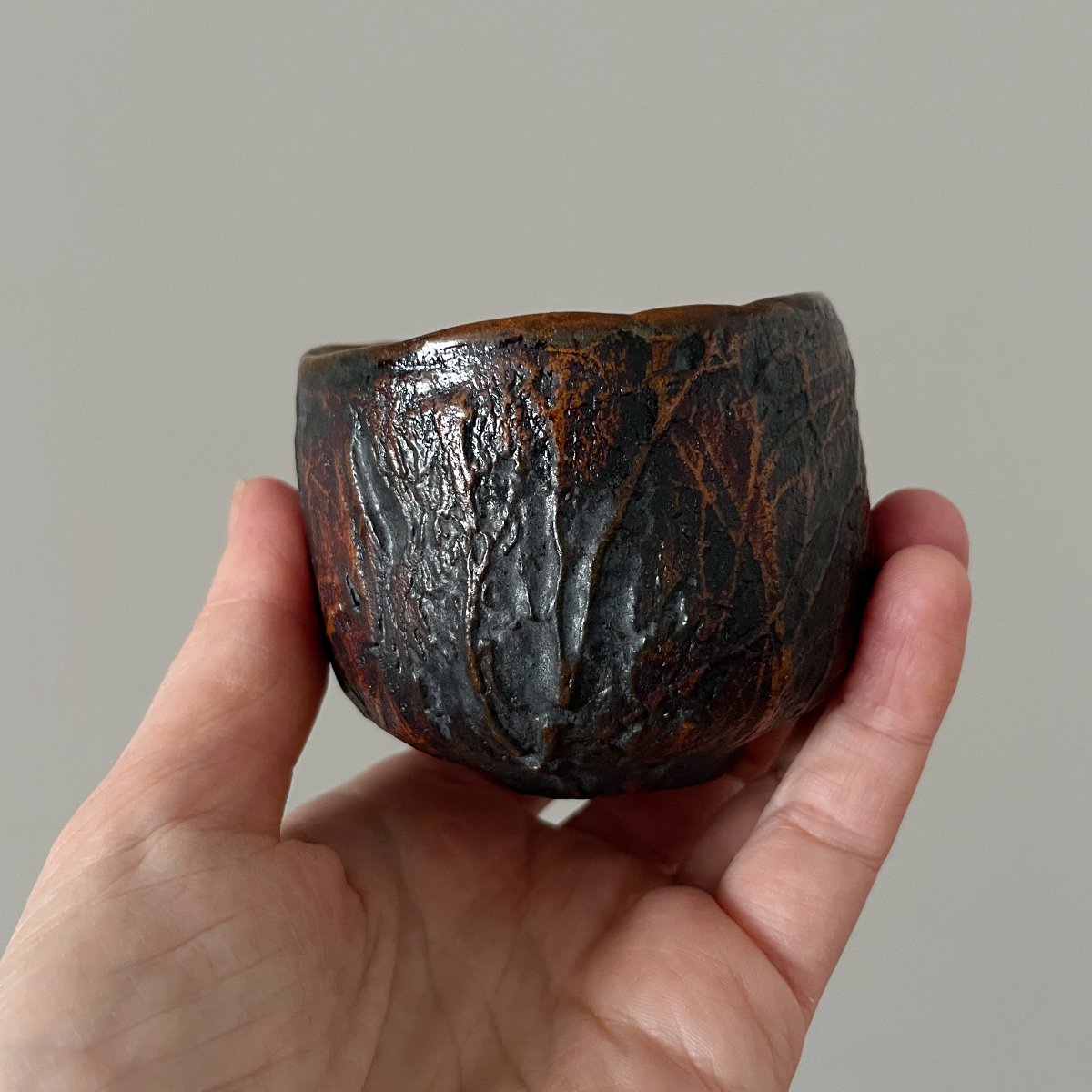 Handcrafted stoneware tea cup held in hand for size reference