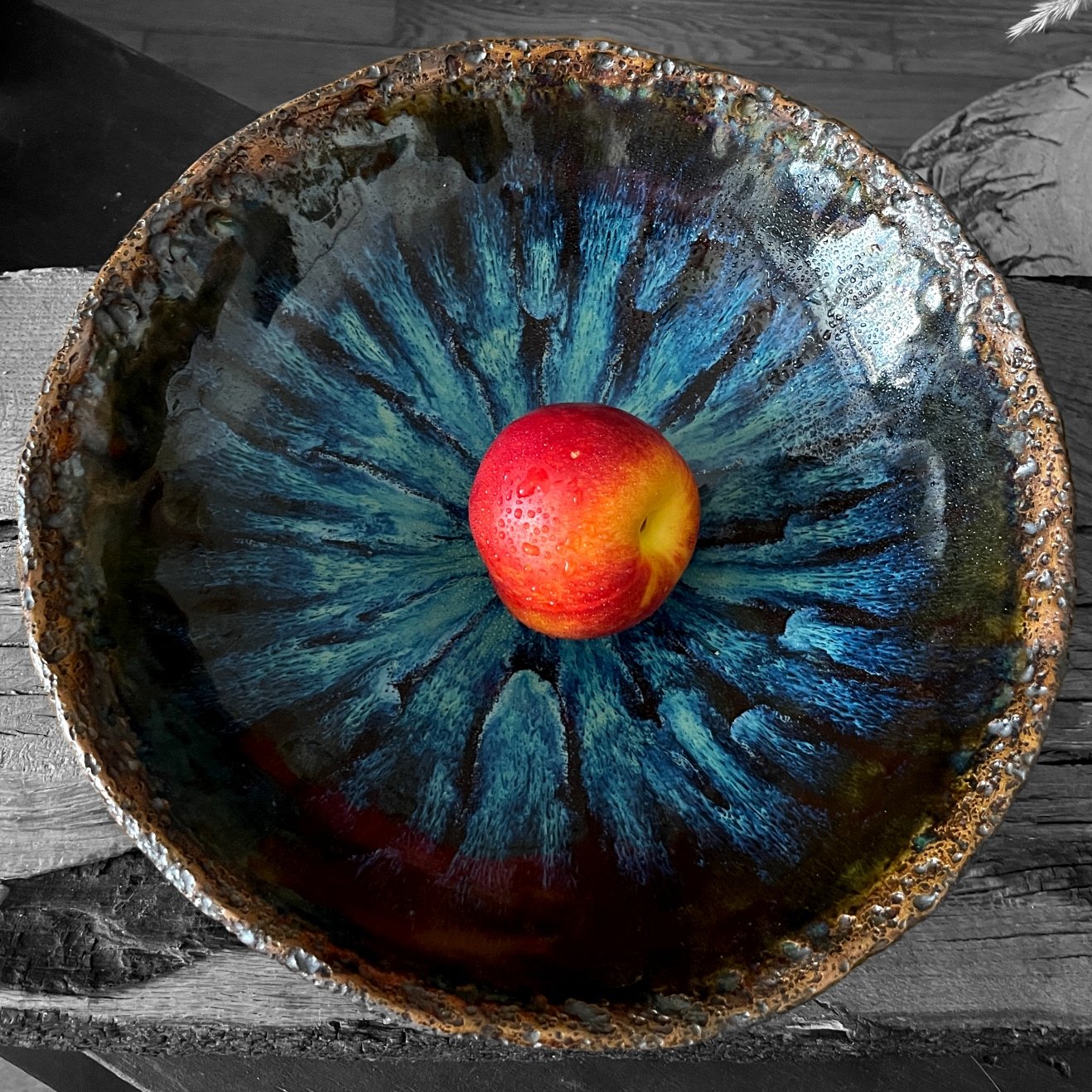 Handmade ceramic fruit bowl with blue crystal glaze holding a nectarine