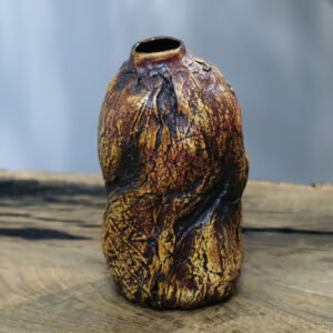 Handbuilt ceramic vase with textured surface standing on wood