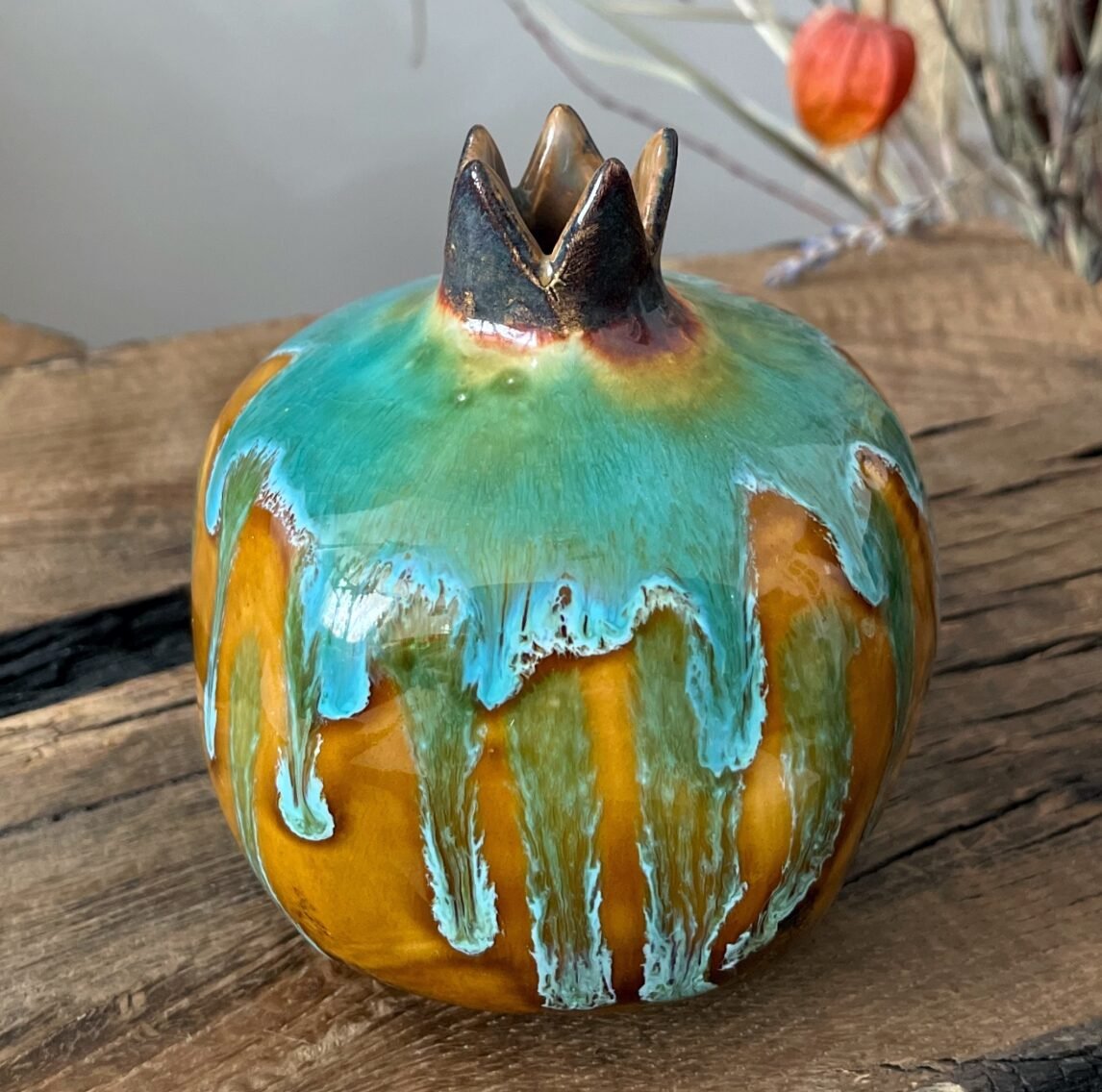 Handmade ceramic pomegranate vase with turquoise drip glaze on wooden table