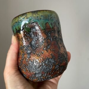 Handmade stoneware coffee cup held in hand for size reference