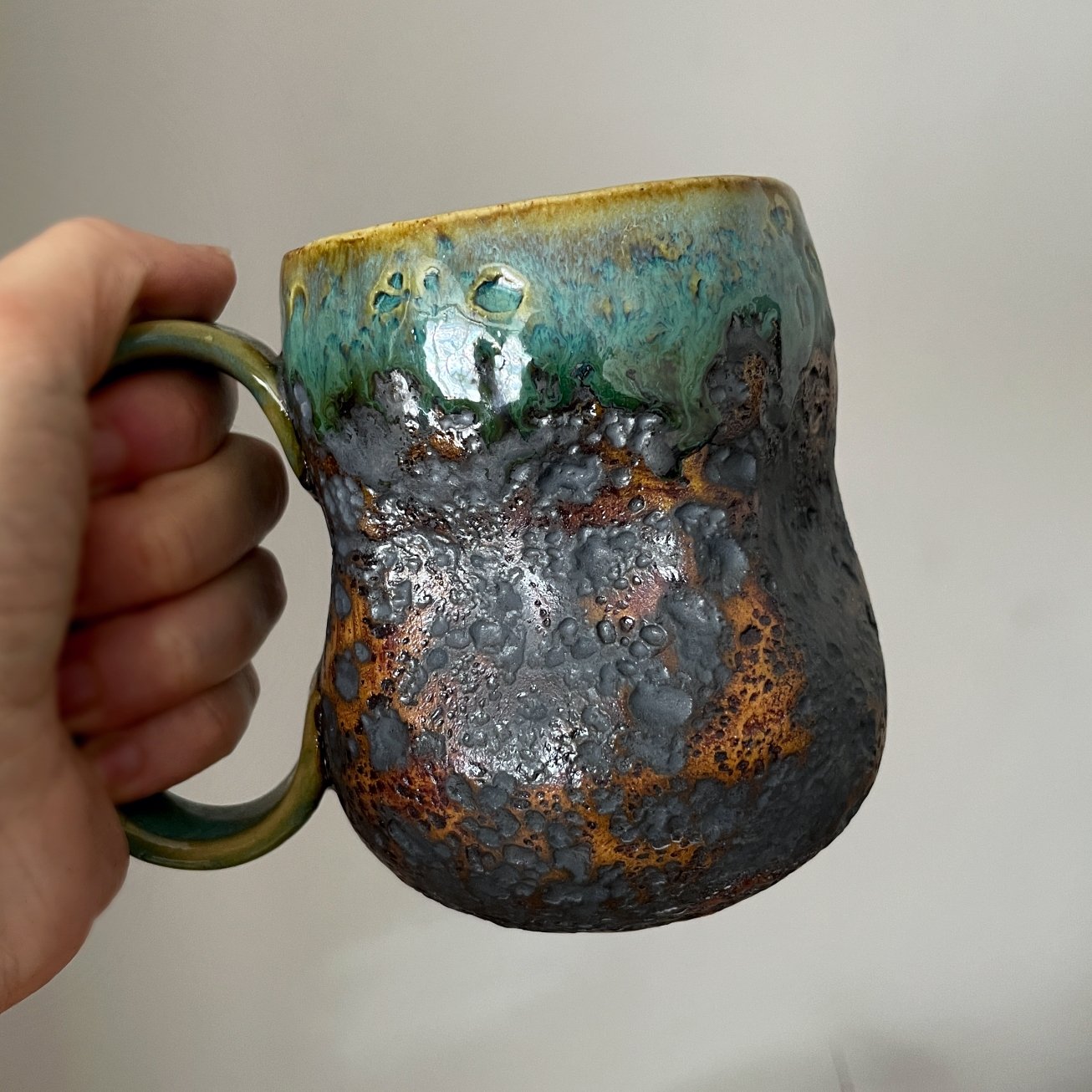 Handmade ceramic mug held in hand showing the glazed interior